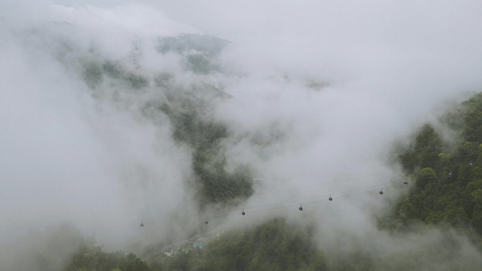 Fog rolling through a green mountain valley, a line of cable cars crossing it